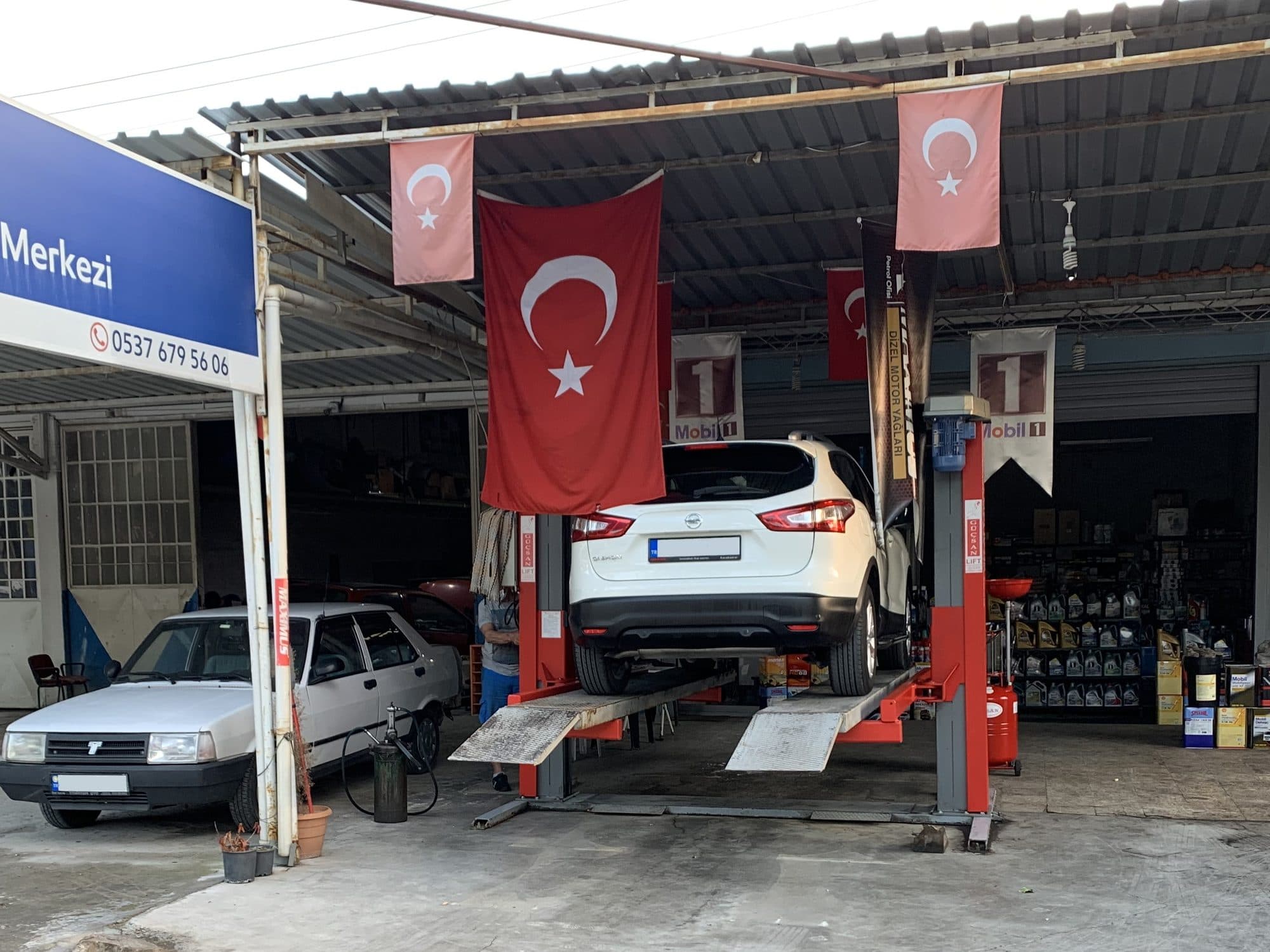 Liftte bakımdaki araç ve arka planda yağ rafları